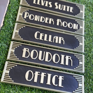 Puede incluir: Cinco letreros decorativos negros y dorados con letras de estilo art d&eacute;co. Los letreros dicen "Elvis Suite", "Tocador", "Bodega", "Tocador" y "Oficina".