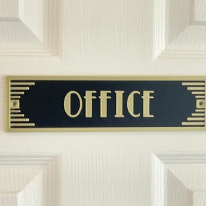 Puede incluir: Un letrero negro con borde dorado y la palabra "OFFICE" en letras doradas.