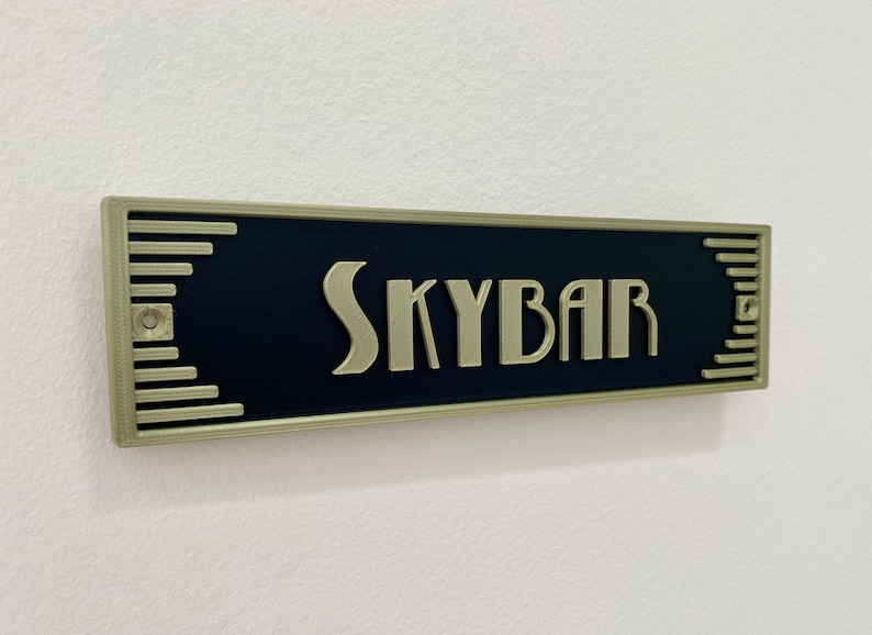 Puede incluir: Un letrero negro con borde dorado y la palabra "SKYBAR" en letras doradas.