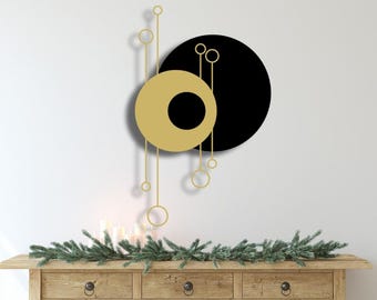 May include: A gold and black abstract wall art piece with a circular design. The piece features a large black circle with a smaller gold circle overlapping it. The gold circle has a smaller black circle inside it. There are also several smaller gold circles connected by thin lines.