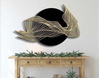 May include: Abstract wall art featuring a black circular background with a gold-colored, wave-like design. The artwork is mounted on a white wall above a wooden console table. The table is decorated with greenery and candles.