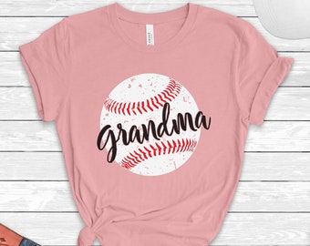 Può includere: Maglietta rosa con un grafico di baseball bianco e la parola "nonna" in corsivo nero.