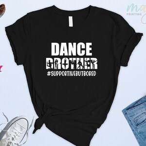 May include: Black t-shirt with white text that reads "Dance Brother #supportivebutbored". The text is surrounded by silhouettes of dancers.