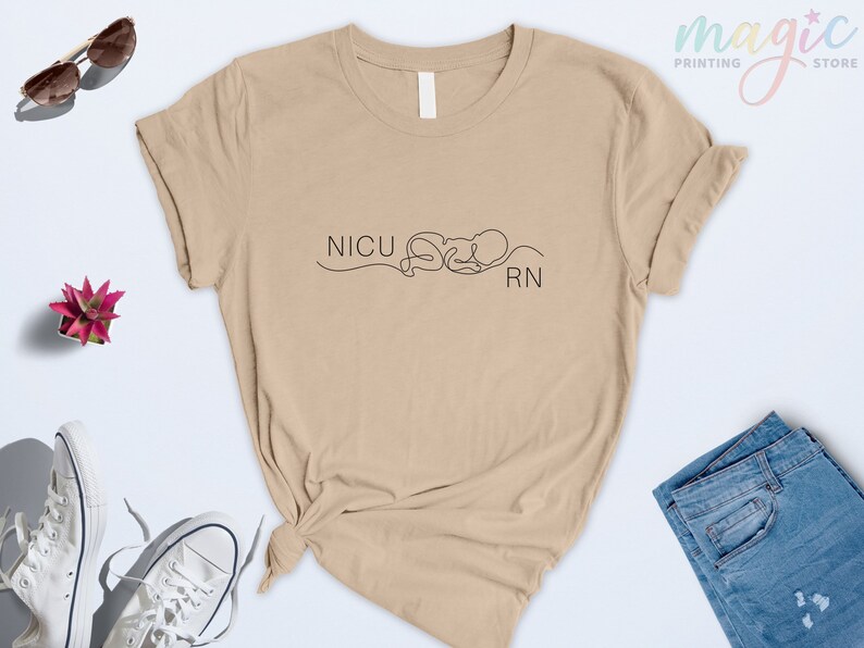 May include: A tan t-shirt with the text "NICU RN" and a simple line drawing of a baby in a swaddle.