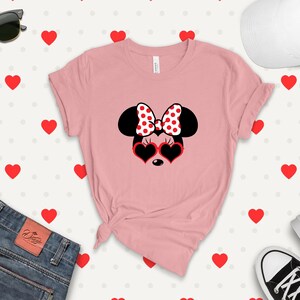 May include: Pink t-shirt with a black and white Minnie Mouse graphic wearing red heart-shaped sunglasses and a red and white polka dot bow.