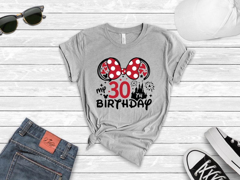 May include: Gray t-shirt with a red and white Minnie Mouse bow, a red number 30, and the text "my 30th birthday" in black. The design also includes a black silhouette of Cinderella's castle and fireworks.