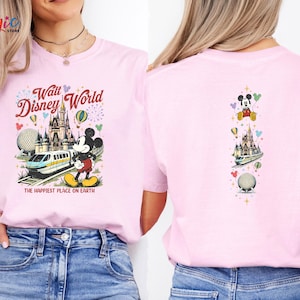 May include: Pale pink t-shirt with a vibrant Walt Disney World graphic. The design includes Mickey Mouse, a monorail, and a castle, with the text "Walt Disney World" and "The Happiest Place on Earth." The back of the shirt has a smaller version of the design.