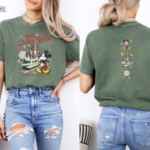 May include: Green t-shirt with a colourful graphic of Mickey Mouse, a train, and a castle with the text "Walt Disney World". The back of the shirt has a vertical design with Mickey Mouse, a castle, and a sphere. The shirt is made of a soft material.