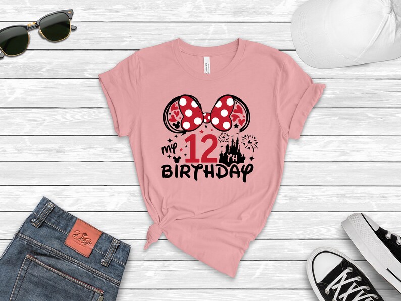 Pu&ograve; includere: Maglietta rosa con un fiocco di Minnie Mouse rosso e bianco, una grafica di castello nero e il testo "my 12th birthday".