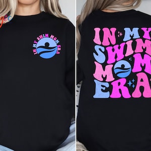 May include: Black sweatshirt with a pink and blue graphic that says "In My Swim Mom Era" on the back and a smaller version of the graphic on the front.