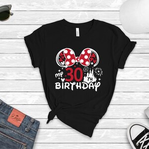 May include: Black t-shirt with a white graphic of Minnie Mouse ears with a red bow and white polka dots. The graphic also includes the text "my 30 birthday" with a white castle and fireworks.
