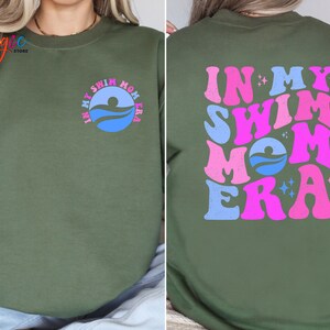 May include: A green sweatshirt with the text "In My Swim Mom Era" in pink and blue lettering with a swimmer graphic. The text is in a retro font.