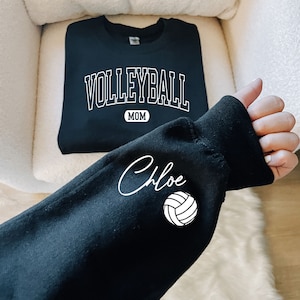 May include: Black sweatshirt with the text "VOLLEYBALL MOM" and a white volleyball graphic. The sleeve has the name "Chloe" written in cursive.