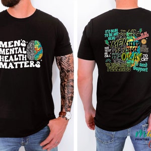 Może przedstawiać: Czarny T-shirt z białym nadrukiem z przodu, kt&oacute;ry m&oacute;wi "Men's Mental Health Matters" i kolorową grafiką m&oacute;zgu. Tył koszulki ma kolorową grafikę z tekstem "W porządku jest prosić o pomoc. Mężczyźni muszą wiedzieć, że w porządku jest płakać. Rozmawiać o swoich uczuciach. Potrzebować wsparcia."