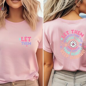 May include: Pink t-shirt with the text "Let them understand, judge you, never doubt your worth, keep shining!" in a colorful, daisy-themed design.