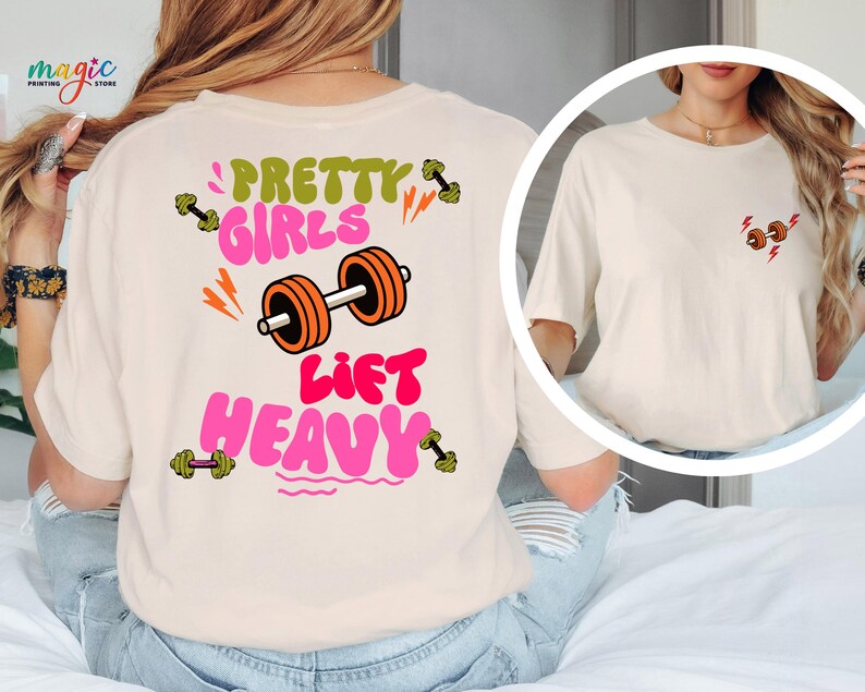Puede incluir: Camiseta color crema con el texto "PRETTY GIRLS LIFT HEAVY" en verde y rosa, junto con gr&aacute;ficos de pesas naranjas y verdes. Una versi&oacute;n m&aacute;s peque&ntilde;a del dise&ntilde;o est&aacute; en la parte delantera. La camiseta es de estilo casual y atl&eacute;tico.