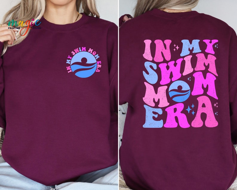 May include: Burgundy sweatshirt with the text "In My Swim Mom Era" in pink and blue lettering on the front and back. The back design features a stylised wave and swimmer graphic.