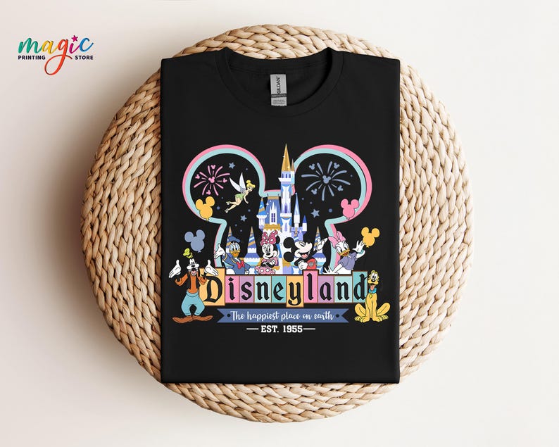 Puede incluir: Camiseta negra con un gr&aacute;fico colorido de Disneyland. El dise&ntilde;o incluye el logotipo de Disneyland, un castillo, fuegos artificiales y varios personajes de dibujos animados. Tambi&eacute;n se incluye el texto "The happiest place on earth - EST. 1955".