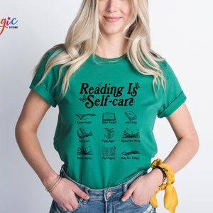 May include: A green t-shirt with the text "Reading Is Self-care" in black. The shirt features a graphic of open books with different phrases, including "Escape Reality", "Better Yourself", "Learn Lots", "Fall in Love", "Think Deeper", "Discover New Worlds", "Reflect Aparty", "Find Peace", and "Make New Friends".