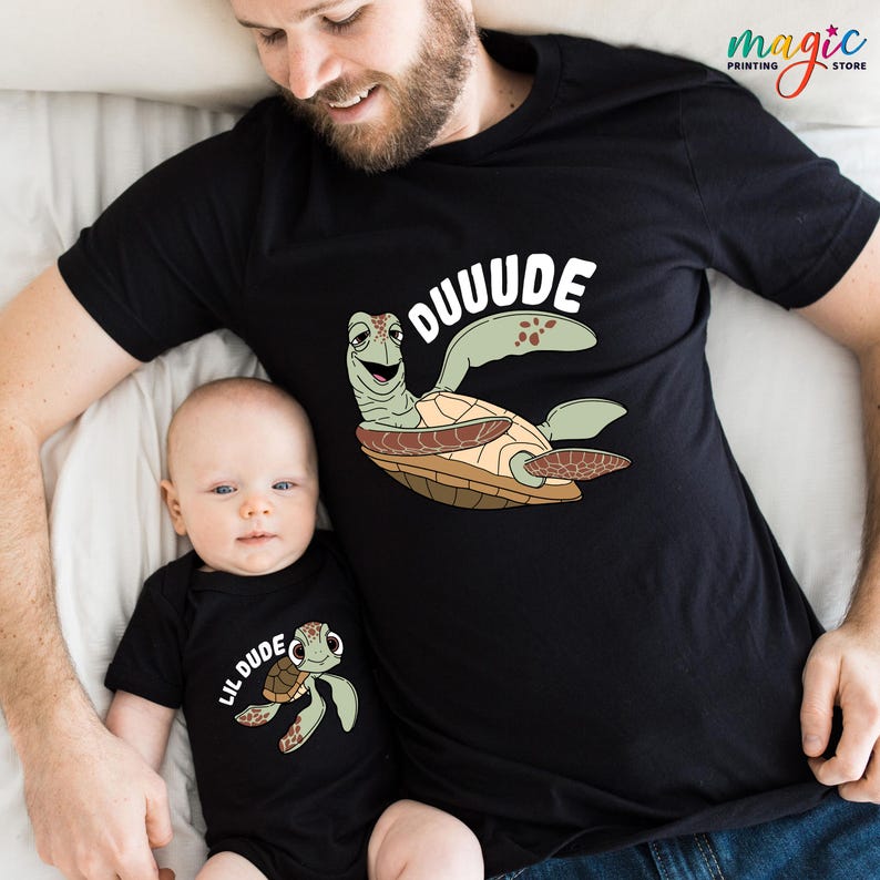 May include: Black t-shirt with a cartoon turtle and the word "OUUUDE" in white. A matching black baby onesie with a turtle graphic and the words "LIL DUDE". The shirts are likely for a parent and child.