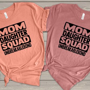 May include: Two peach and mauve t-shirts with black text that reads "Mom Daughter Squad Unbreakablebond".