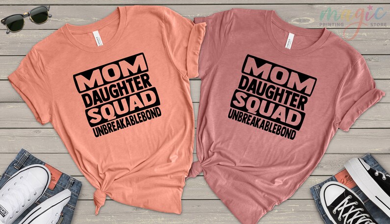 May include: Two peach and mauve t-shirts with black text that reads "Mom Daughter Squad Unbreakablebond".