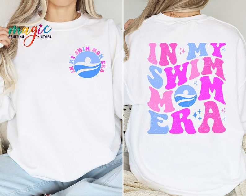 May include: White sweatshirt with a blue and pink graphic that says "In My Swim Mom Era" on the back. The front of the sweatshirt has a smaller blue graphic with a swimmer and the words "In My Swim Mom Era".
