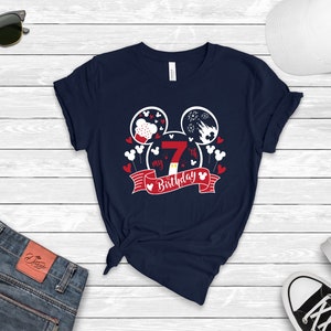 以下が含まれることがあります： 白いミッキーマウスの頭のデザインが施されたネイビーブルーのTシャツ。デザインには、赤い白の誕生日バナーに数字の7と「my 7th birthday」の文字が書かれています。