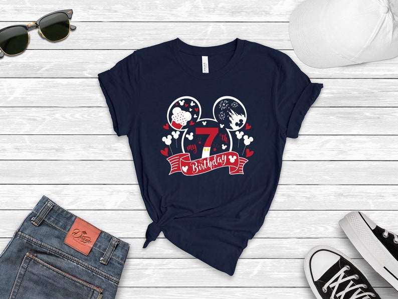 以下が含まれることがあります： 白いミッキーマウスの頭のデザインが施されたネイビーブルーのTシャツ。デザインには、赤い白の誕生日バナーに数字の7と「my 7th birthday」の文字が書かれています。