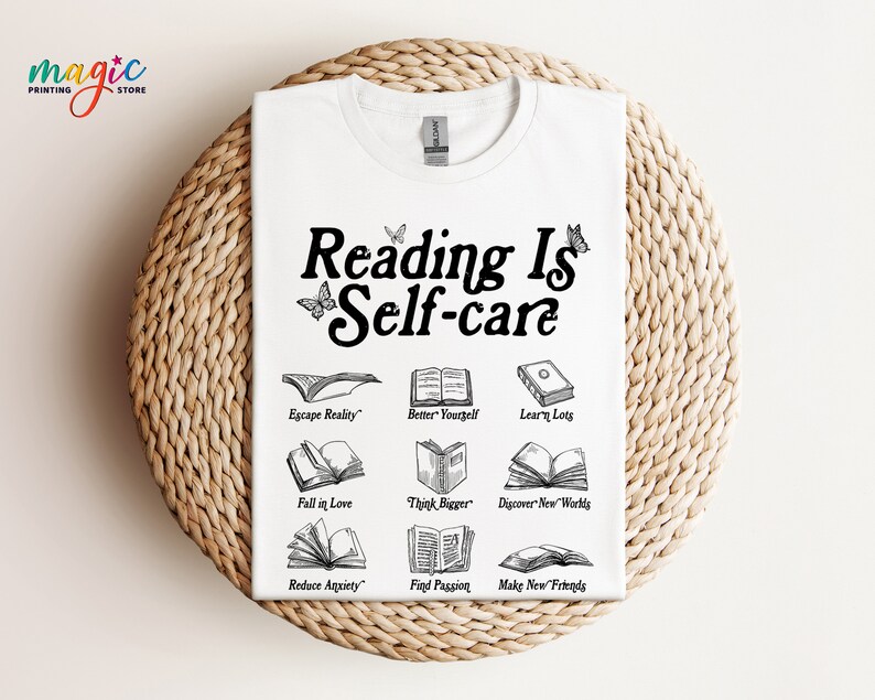 May include: White t-shirt with black text that reads "Reading Is Self-care" and illustrations of open books with text describing the benefits of reading, such as "Escape Reality", "Better Yourself", "Learn Lots", "Fall in Love", "Think Bigger", "Discover New Worlds", "Reduce Anxiety", "Find Passion", and "Make New Friends".