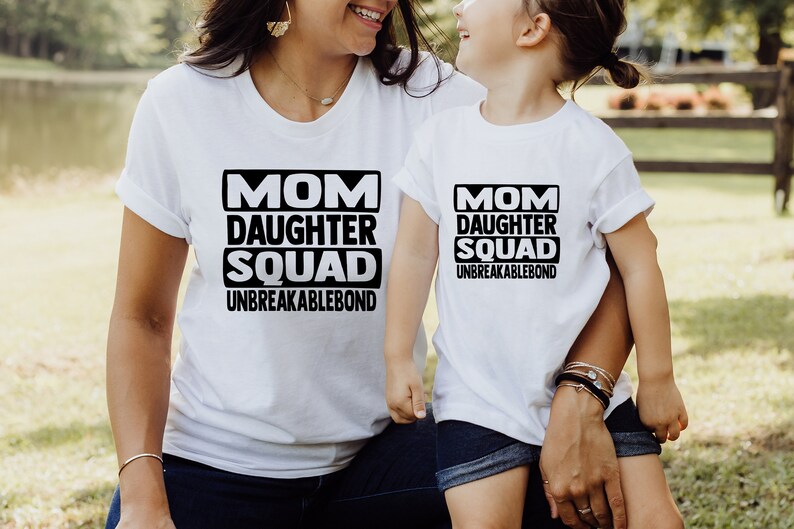 May include: White t-shirts with black text that reads "Mom Daughter Squad Unbreakablebond". The shirts are worn by a woman and a young girl.