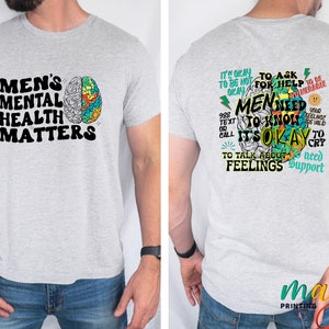 Może przedstawiać: Szara koszulka z kolorowym grafiką m&oacute;zgu i tekstem "Men's Mental Health Matters" z przodu. Z tyłu koszulka ma kolorową grafikę m&oacute;zgu z tekstem "W porządku jest prosić o pomoc. Mężczyźni muszą wiedzieć, że w porządku jest rozmawiać o uczuciach. Potrzebujesz wsparcia."