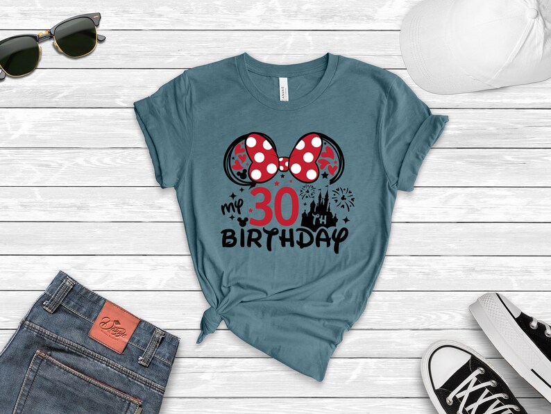May include: Teal blue t-shirt with a black and red Minnie Mouse ears design. The ears have white polka dots. The text "my 30th birthday" is printed below the ears.