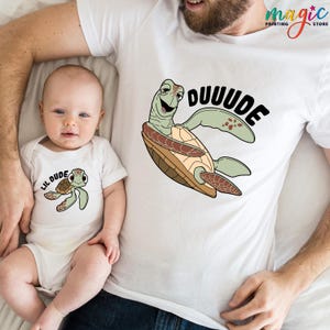 May include: White t-shirts and baby bodysuit with matching turtle graphic. The adult shirt features a large turtle with the word "DUUUDE" in black. The baby bodysuit has a smaller turtle and the words "LIL DUDE".