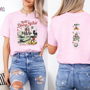 May include: Pale pink t-shirt with a Walt Disney World graphic. The front shows Mickey Mouse, a monorail, and Cinderella's castle, with the text "Walt Disney World" and "The Happiest Place on Earth". The back has a vertical design with Mickey Mouse and other Disney icons.