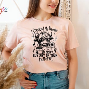May include: A light pink t-shirt with a black graphic of a Highland cow wearing sunglasses and holding a sunflower and coffee cup. The text reads "I checked my receipt, I didn't buy any of your bullshit!"