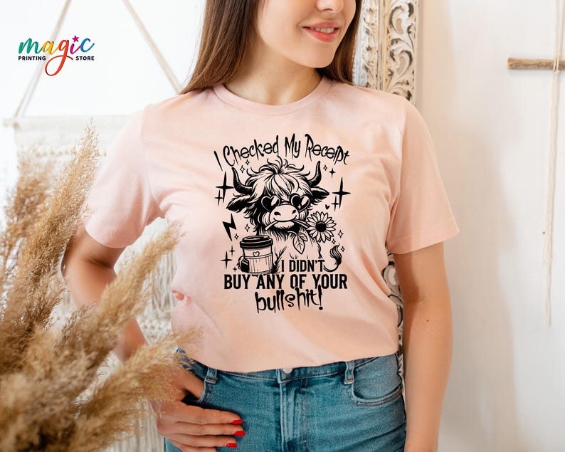 May include: A light pink t-shirt with a black graphic of a Highland cow wearing sunglasses and holding a sunflower and coffee cup. The text reads "I checked my receipt, I didn't buy any of your bullshit!"