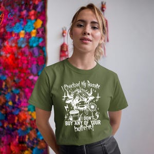 May include: Olive green t-shirt with a white graphic of a Highland cow, coffee cup, and flower. The text on the shirt reads "I checked my receipt, I didn't buy any of your bullshit!" The shirt is a casual style.