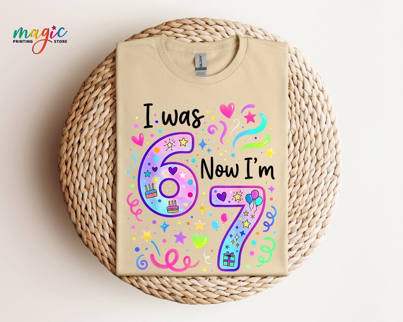 May include: A beige t-shirt featuring the phrase "I was 6, Now I'm 7" in a vibrant, celebratory design. The graphic includes hearts, stars, confetti, and cake illustrations, ideal for a child's seventh birthday.