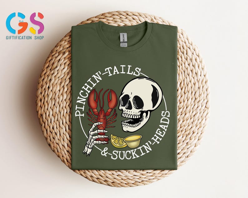K&ouml;nnte beinhalten: Gr&uuml;nes T-Shirt mit einer wei&szlig;en Grafik eines Sch&auml;dels, der einen Hummer mit dem Text "Pinchin'-Tails &-Suckin'-Heads" h&auml;lt.