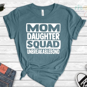 May include: A teal blue t-shirt with white text that reads "Mom Daughter Squad Unbreakablebond".