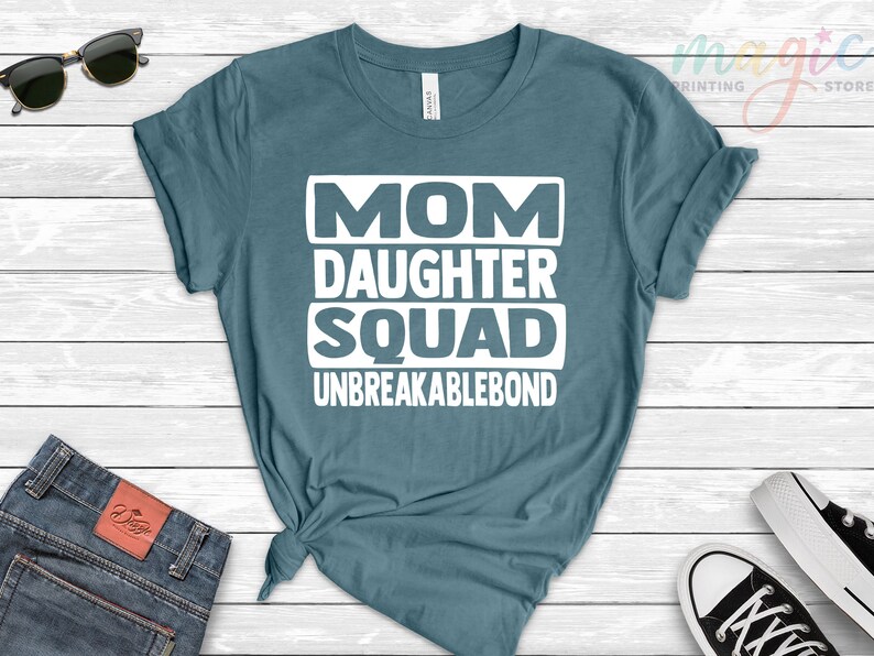 May include: A teal blue t-shirt with white text that reads "Mom Daughter Squad Unbreakablebond".
