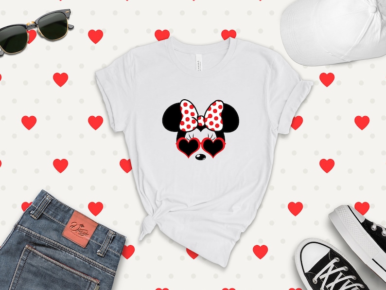 May include: White t-shirt with a black and white illustration of Minnie Mouse wearing red heart-shaped sunglasses and a red and white polka dot bow. The background is a white pattern of red hearts.