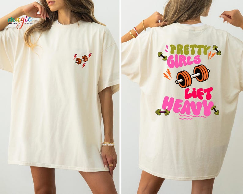 Puede incluir: Camiseta color crema con un peque&ntilde;o gr&aacute;fico de mancuernas y un rayo en la parte delantera. La parte trasera presenta el texto "Pretty Girls Lift Heavy" con un gr&aacute;fico de mancuernas. El dise&ntilde;o utiliza colores naranja, verde y rosa.