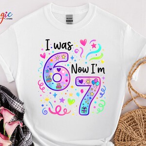 May include: White t-shirt featuring the text "I was 6, Now I'm 7" in a vibrant, multi-colored design. The graphic includes the numbers 6 and 7, along with hearts, stars, and confetti, perfect for a birthday.