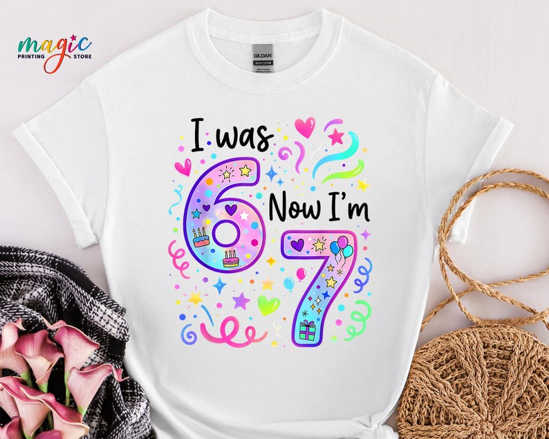 May include: White t-shirt featuring the text "I was 6, Now I'm 7" in a vibrant, multi-colored design. The graphic includes the numbers 6 and 7, along with hearts, stars, and confetti, perfect for a birthday.