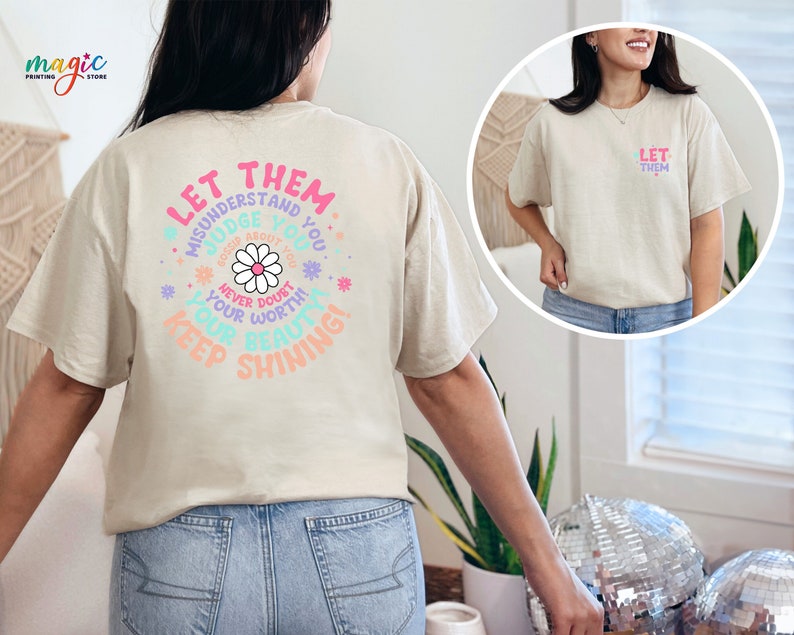 May include: A beige t-shirt with a colorful graphic on the back that says "Let them misunderstand you, judge you, gossip about you, never doubt your worth, you are beautiful, keep shining!" The graphic features a daisy flower and other floral elements.