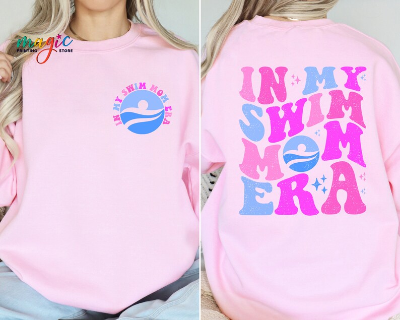 May include: Pink sweatshirt with the text "In My Swim Mom Era" in a retro font with blue, pink, and white colours. The text is on the back of the sweatshirt. The front of the sweatshirt has a smaller version of the text in a circle.
