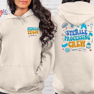 May include: Cream-colored hoodie with the text "STERILE TECH Sophia" on the front and "STERILE PROCESSING CREW" with medical-themed illustrations on the back. The design features blue, orange, and white text.