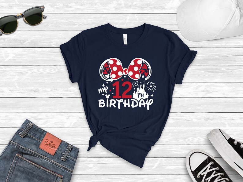 Pu&ograve; includere: Una maglietta blu navy con una grafica bianca di un fiocco rosso e bianco a pois, il numero 12, un castello e fuochi d'artificio. Il testo "my 12th birthday" &egrave; stampato sotto la grafica.